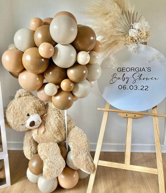 Panel de bienvenida con globos marrones, flores y oso