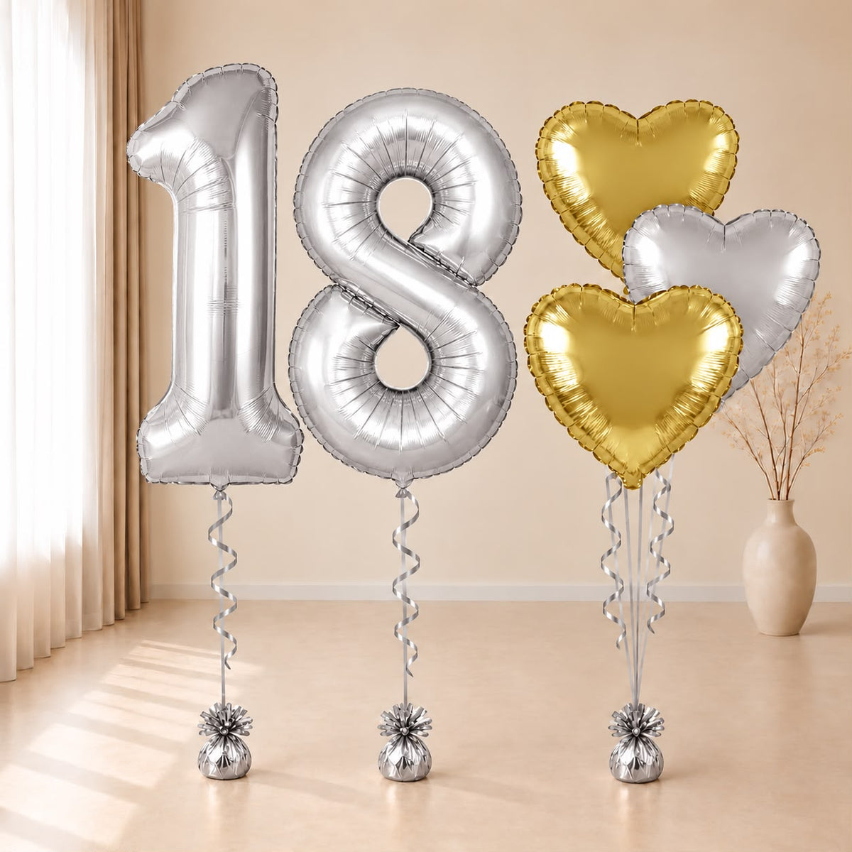 Composición de globos con números 18 plateados y corazones dorados y plateado, con cintas y contrapesos plateados.