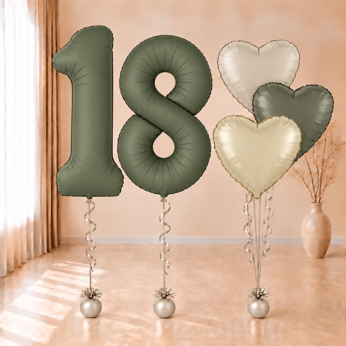 Composición de globos con números 18 verde oliva y corazones en verde y tonos crema, con cintas y contrapesos claros.