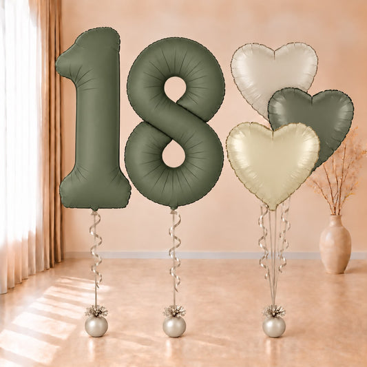 Composición de globos con números 18 verde oliva y corazones en verde y tonos crema, con cintas y contrapesos claros.