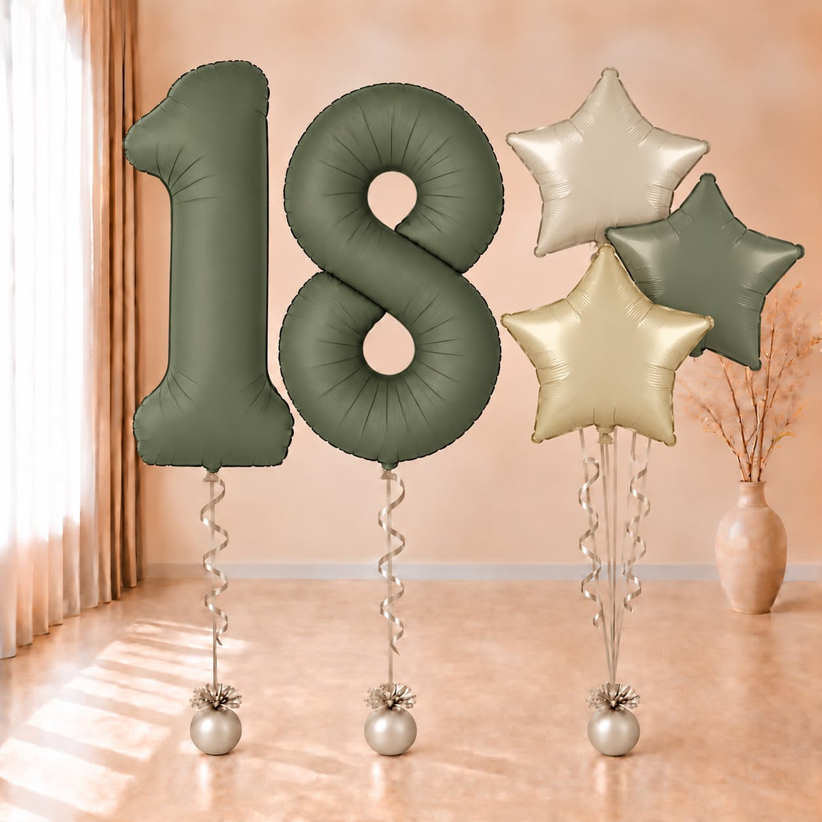 Composición de globos con números 18 verde oliva y estrellas en verde y tonos crema, con cintas y contrapesos claros.